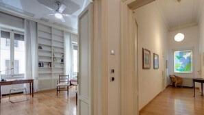 Une pièce spacieuse dotée d’un plancher en bois, d’un bureau avec une chaise, d’une bibliothèque et d’une grande fenêtre offrant une belle vue.
