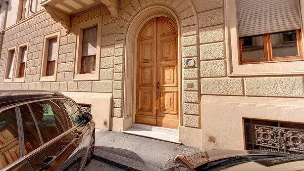 Un bâtiment doté d’une grande porte en bois, avec une voiture garée devant et un petit balcon agrémenté de balustrades.