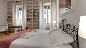 Un lit bien fait, avec du linge de lit blanc, une bibliothèque remplie de livres et un tableau accroché au mur.