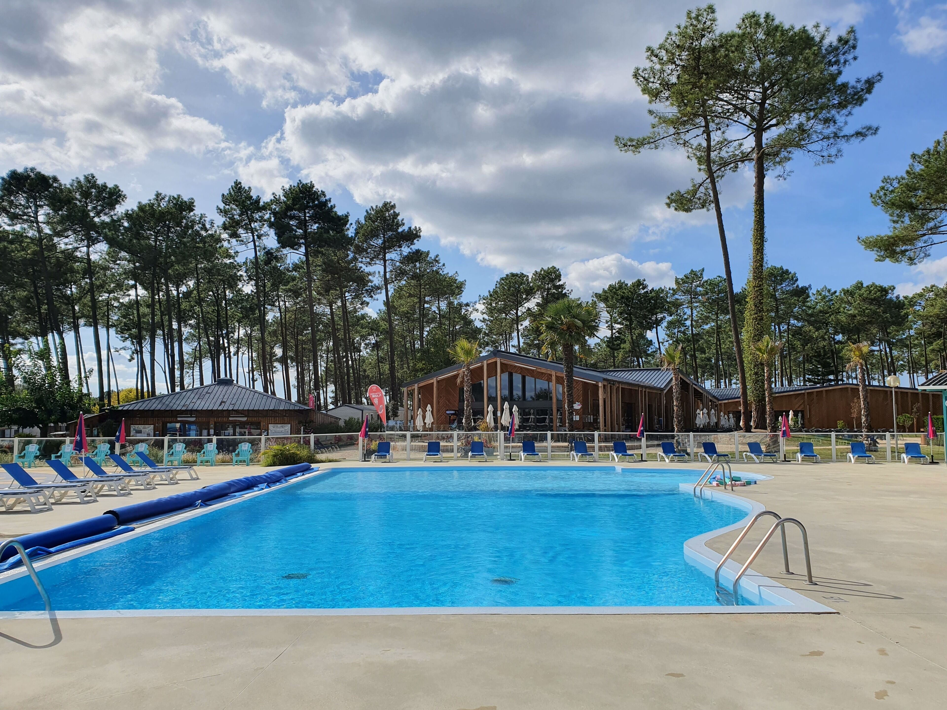 Une piscine avec des chaises longues et un bâtiment en bois doté de grandes fenêtres.