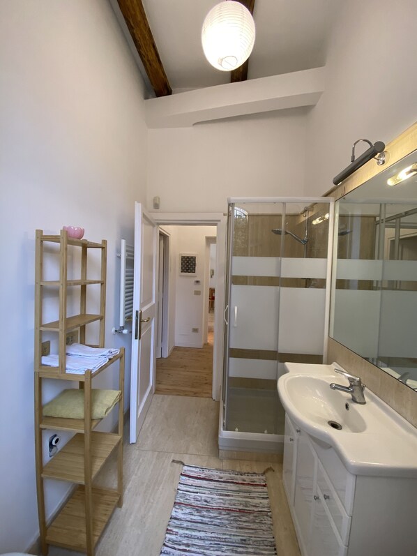 Ein Badezimmer mit Holzregal, Dusche, Waschbecken und Spiegel.