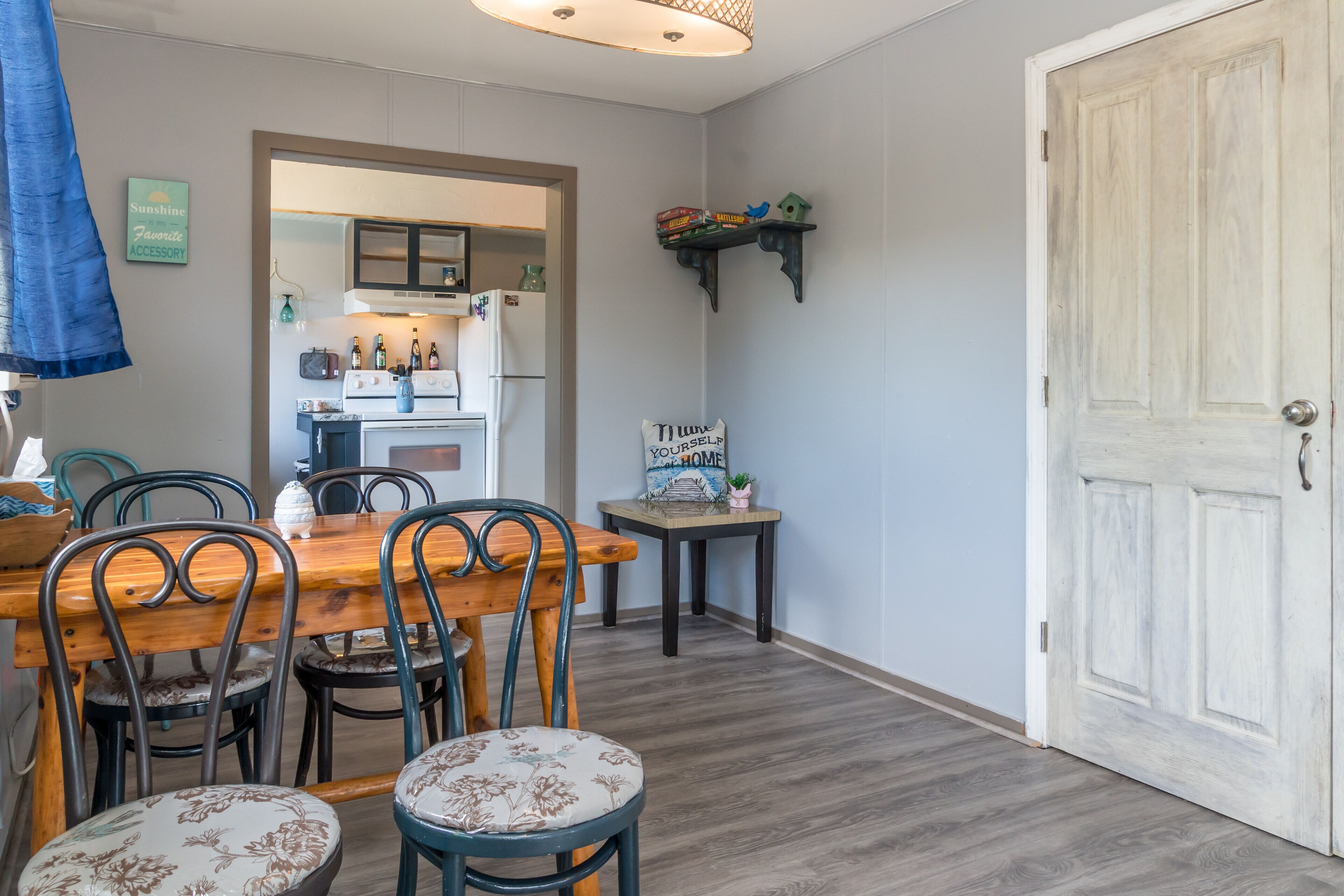 Un comedor con una mesa y sillas de madera, una cocina al fondo y una puerta blanca.