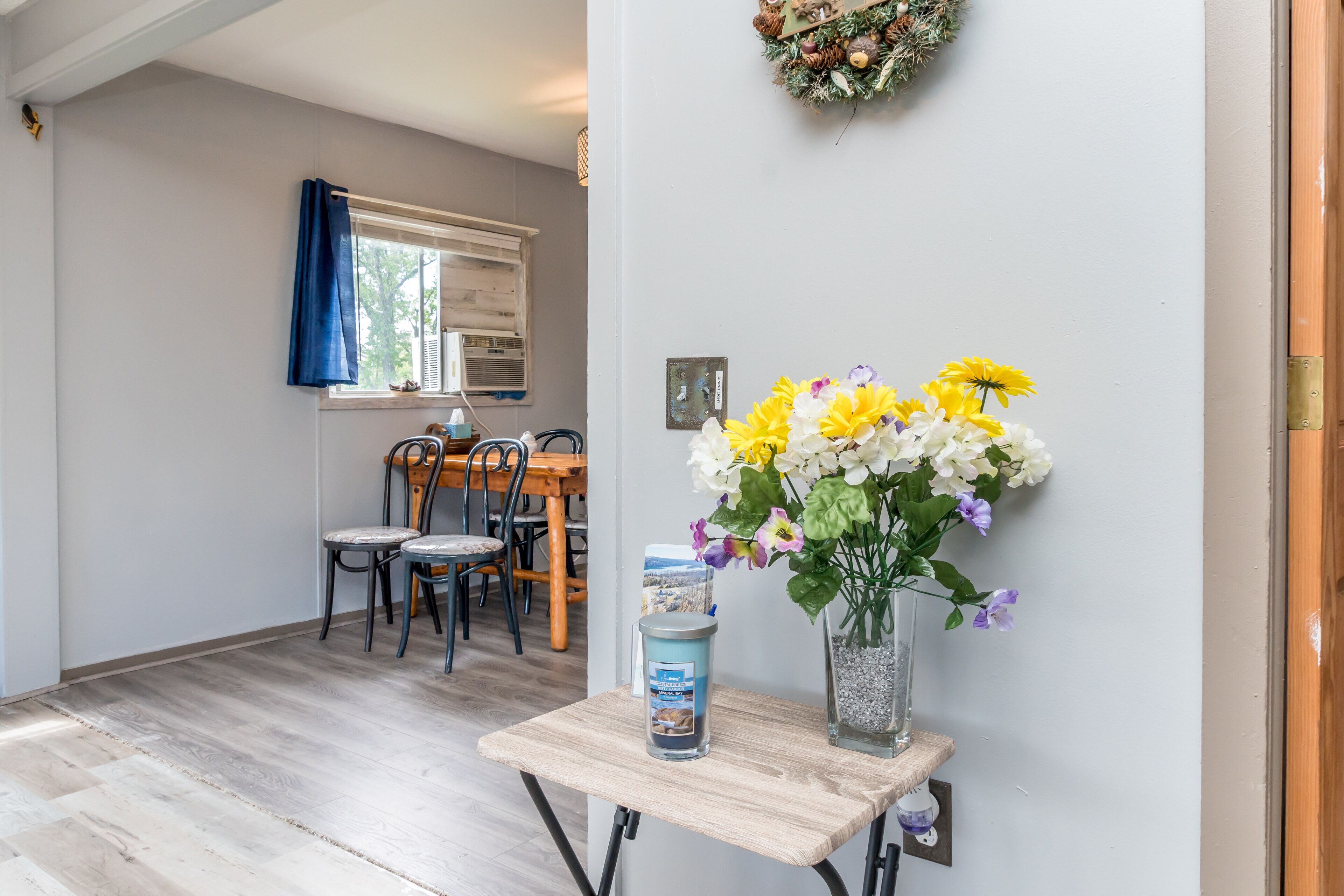 Un comedor con una mesa y sillas de madera, un jarrón con flores y una mesita con un recipiente.