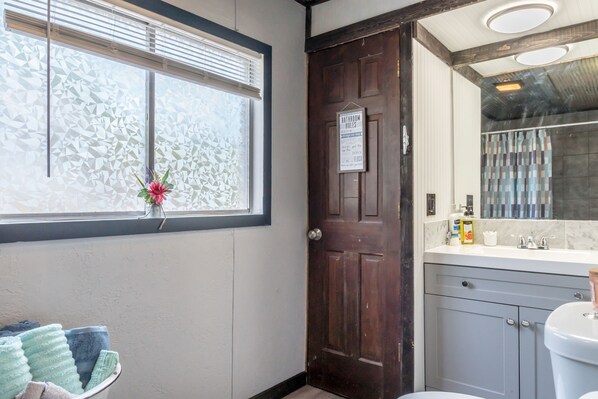 Een badkamer met een houten deur, een raam met gezandstraald glas, een wastafel en een toilet.