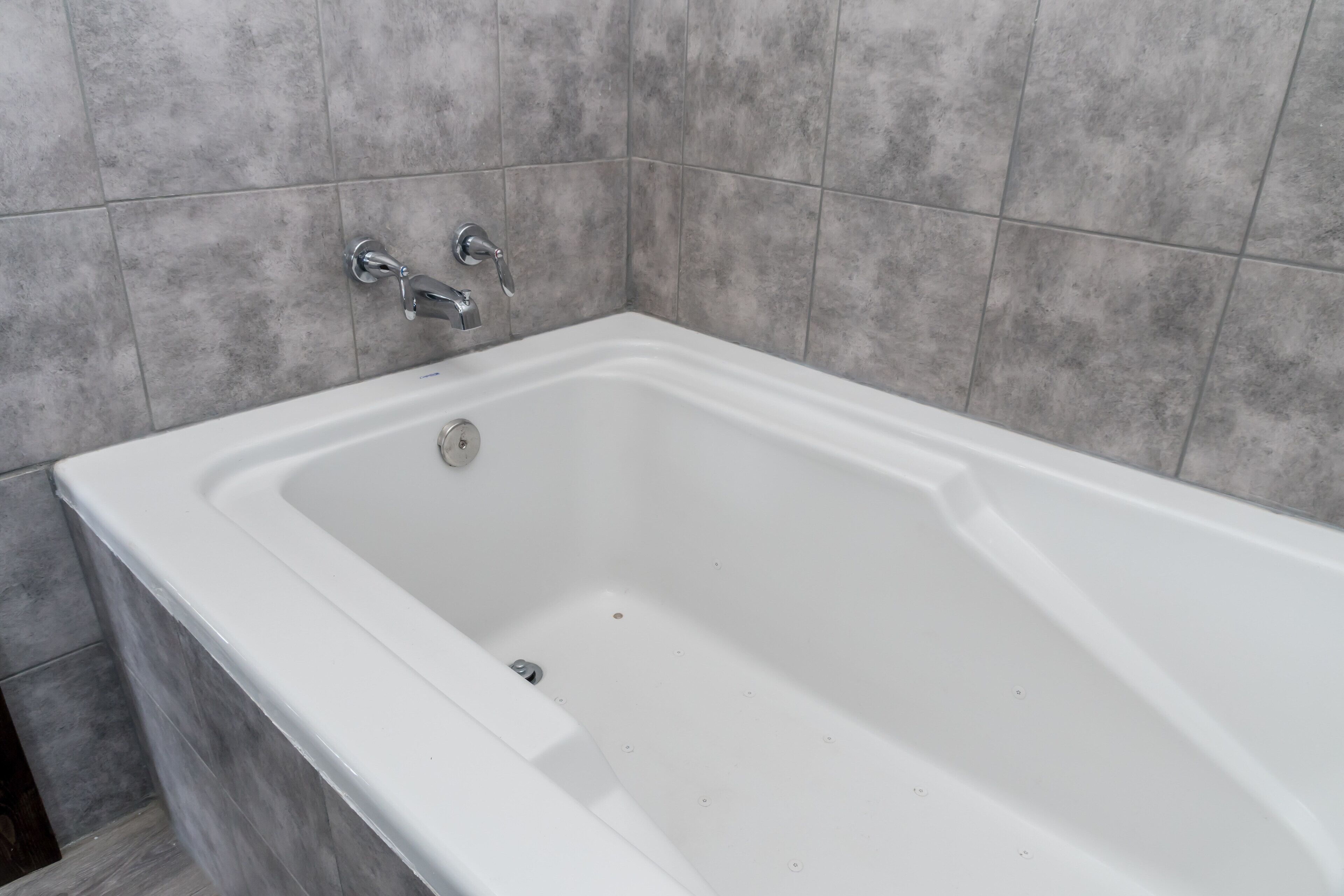 A white bathtub with a chrome faucet and a single control knob, set against a tiled wall.