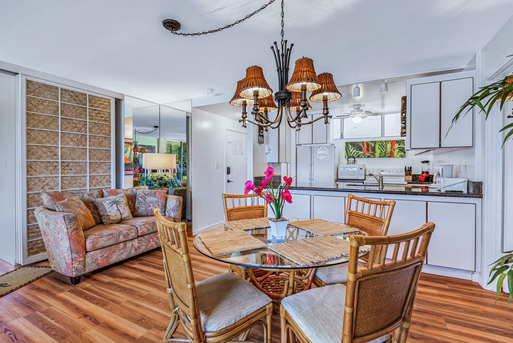 A modern kitchen with white cabinets, a dining table with wicker chairs, and a hanging light fixture.