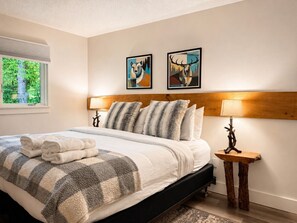 Un lit bien fait, recouvert d’une couverture à carreaux, deux tableaux représentant des animaux encadrés au mur et une lampe de chevet.