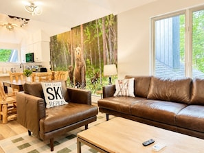A living room with a brown leather sofa, a brown leather armchair, a wooden coffee table, and a painting of a forest scene.