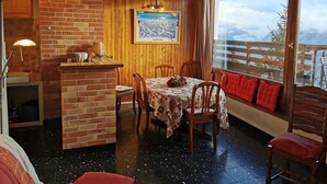 A cozy dining area with a brick wall, wooden ceiling, and a table set for four. A framed picture hangs on the wall, and a window offers a view of the outdoors.
