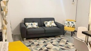 A living room with a grey sofa, yellow ottoman, and a geometric patterned rug.