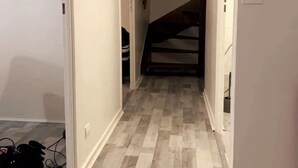 A narrow hallway with a wooden floor, a staircase at the end, and a light fixture on the left.