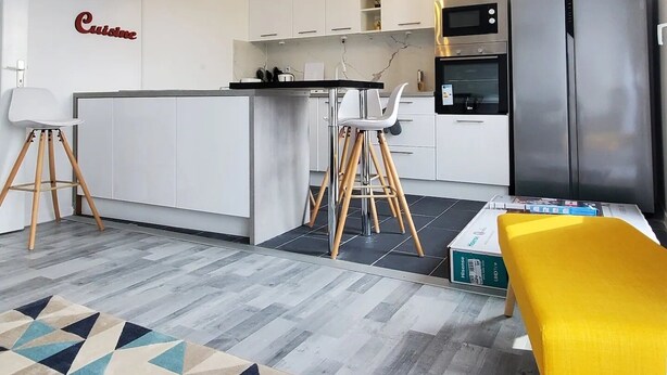 A modern kitchen with white cabinets, a central island, a stainless steel refrigerator, and a geometric patterned rug.