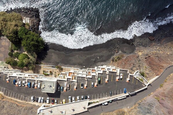 An aerial view of a parking lot adjacent to a rocky coastline with waves crashing onto the shore.