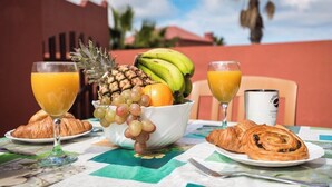 A breakfast setting with a fruit bowl, croissants, and glasses of orange juice on a table. - Home2Book Oasis Paradise Home Fuerteventura (Corralejo)