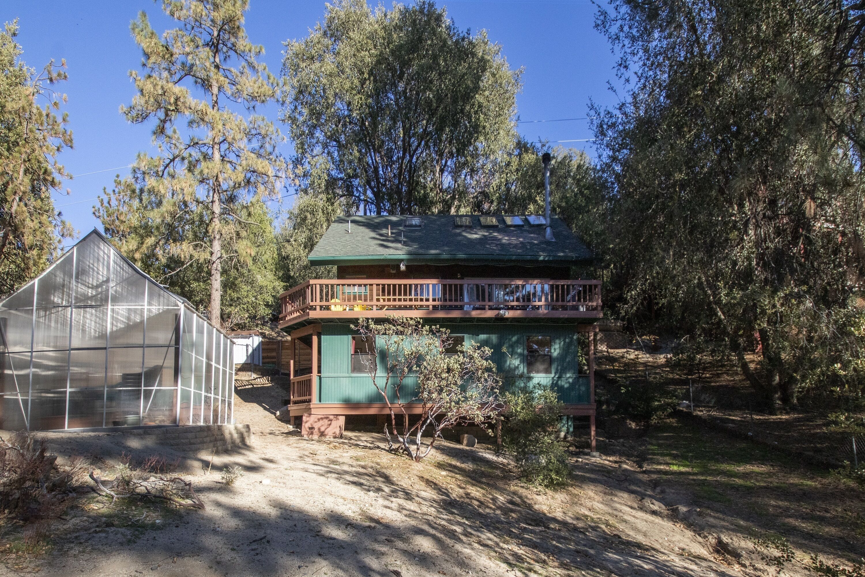 Une maison à deux étages, avec une façade verte et un balcon à l’étage supérieur.