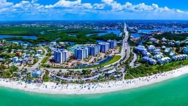 Vista aérea de un complejo turístico costero con un paseo marítimo central, acceso directo a la playa y vegetación circundante.