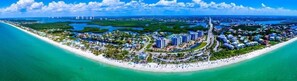 An aerial view of a coastal resort with a central promenade, beachfront, and surrounding greenery.