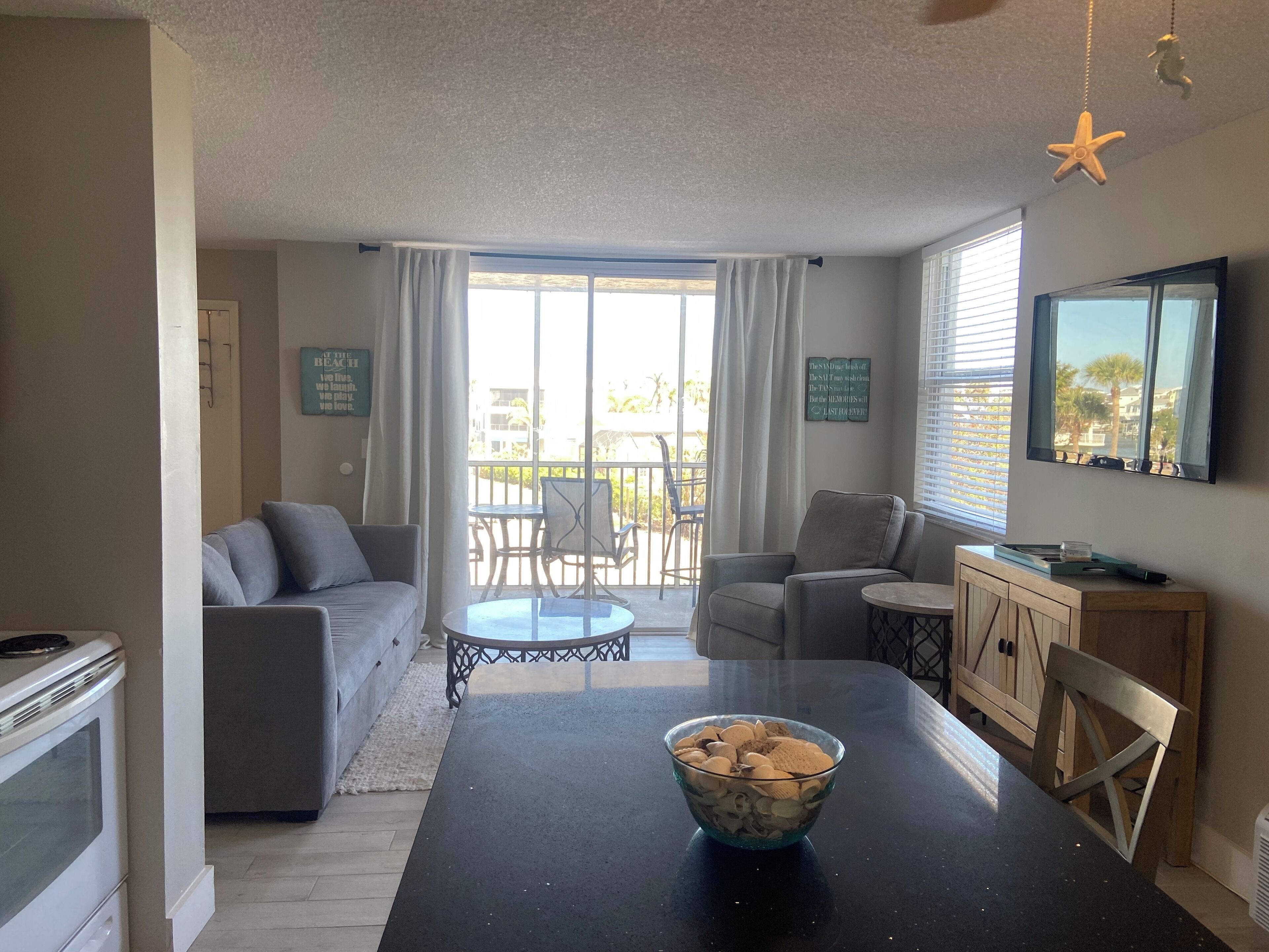 Ein Wohnzimmer mit einer Couch, Sesseln, einem Esstisch mit einer Schüssel Frühstücksflocken, einem Fernseher und einem Balkon mit Aussicht.