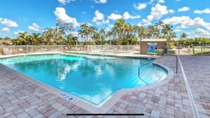 Una piscina con un borde empedrado, rodeada de palmeras y un cielo despejado.