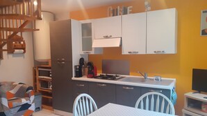 Een compacte keuken met moderne apparatuur, een eethoek met een tafel en stoelen, en een trap naar een hoger niveau.