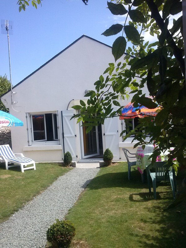 A house with a white exterior, a gravel pathway leading to the entrance, and a small garden area with a table and chairs. - fisherman's house (Perros-Guirec)