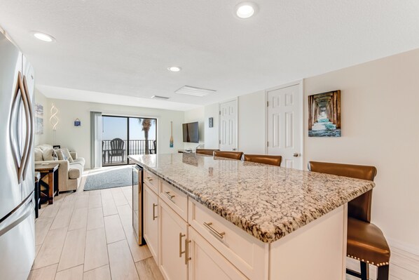 A modern kitchen with a granite countertop, white cabinets, and a dining area with brown leather chairs. - Modern Décor and Ocean Galore! Newly Renovated Oceanfront Condo sleeps 6 (Ormond Beach)