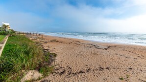 A beach with a wooden walkway leading to a building, a clear sky, and waves in the distance.