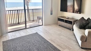 Ein Wohnzimmer mit einer großen SchiebeglasTür, die auf einen Balkon mit Blick auf den Strand führt.