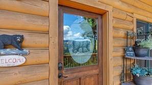 L'ingresso di una baita in legno, decorata con un'immagine di un orso, un cartello di benvenuto e una porta in vetro che riflette il paesaggio circostante.