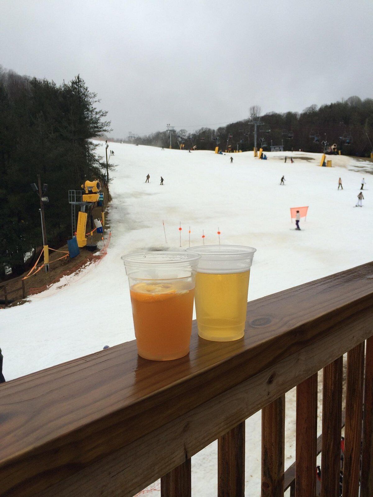 A snowy ski slope with people skiing and a wooden railing in the foreground.