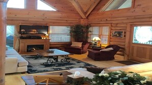Un accogliente interno di una baita in legno con camino, posti a sedere comodi e televisore.