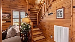 Interno di una baita in legno con una scala, un divano, una lampada e un quadro appeso al muro.