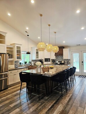 Una cocina moderna con una isla central, luces colgantes y un refrigerador de acero inoxidable.