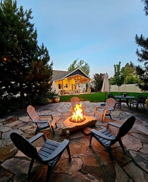 A stone patio with a fire pit and Adirondack chairs. - Luxury Retreat-gourmet kitchen, playhouse, hot tub, & steam shower (Layton)