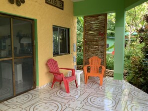 A covered porch with two plastic chairs, a tiled floor, and a green wall with a window.