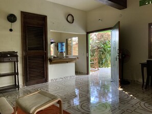 A spacious room with a tiled floor, a wooden bench, a water dispenser, and a view of the outdoors.