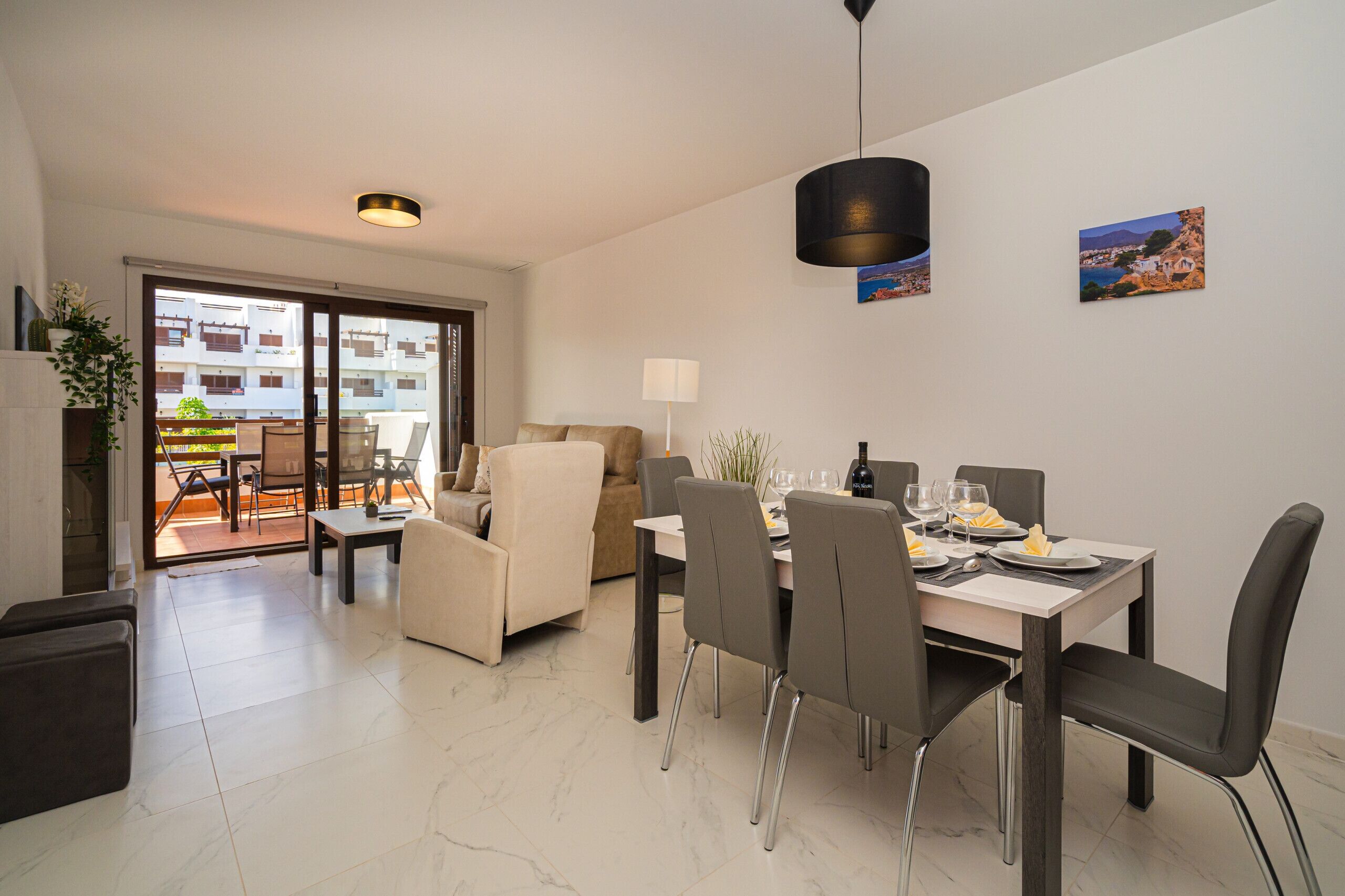 Un comedor moderno con una mesa dispuesta para seis personas, un sofá y vistas al balcón exterior.