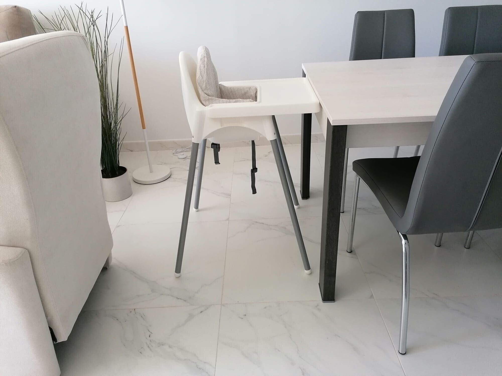 A modern dining area with a white table and black chairs, a potted plant, and a marble floor.