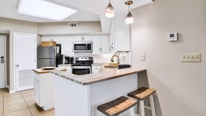 A modern kitchen with white cabinets, stainless steel appliances, a marble countertop, and two bar stools. - Windward Pointe 604 | Spacious, Update, Beach Front! (Orange Beach)