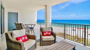 A balcony with wicker furniture, a small table, and a view of the beach and ocean. - Windward Pointe 604 | Spacious, Update, Beach Front! (Orange Beach)