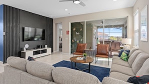 A modern living room with a flat-screen TV, grey sofas, a coffee table, and a ceiling fan.
