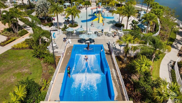 A water park with a large blue pool, slides, and palm trees.