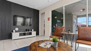 A modern living room with a flat-screen TV, a coffee table with a magazine, a potted plant, and leather chairs.