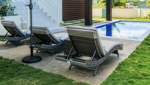 Et moderne hus med to etager, en swimmingpool, udendørs siddepladser og en trappe til en balkon.