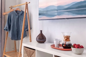 A room with a wooden hanger rack, a coffee maker, a vase, and a bowl of strawberries.