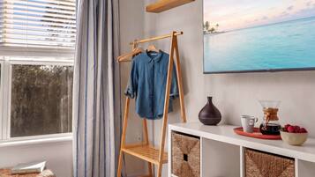 A room with a wooden clothes rack, a white console table, a TV, and a window with blinds.