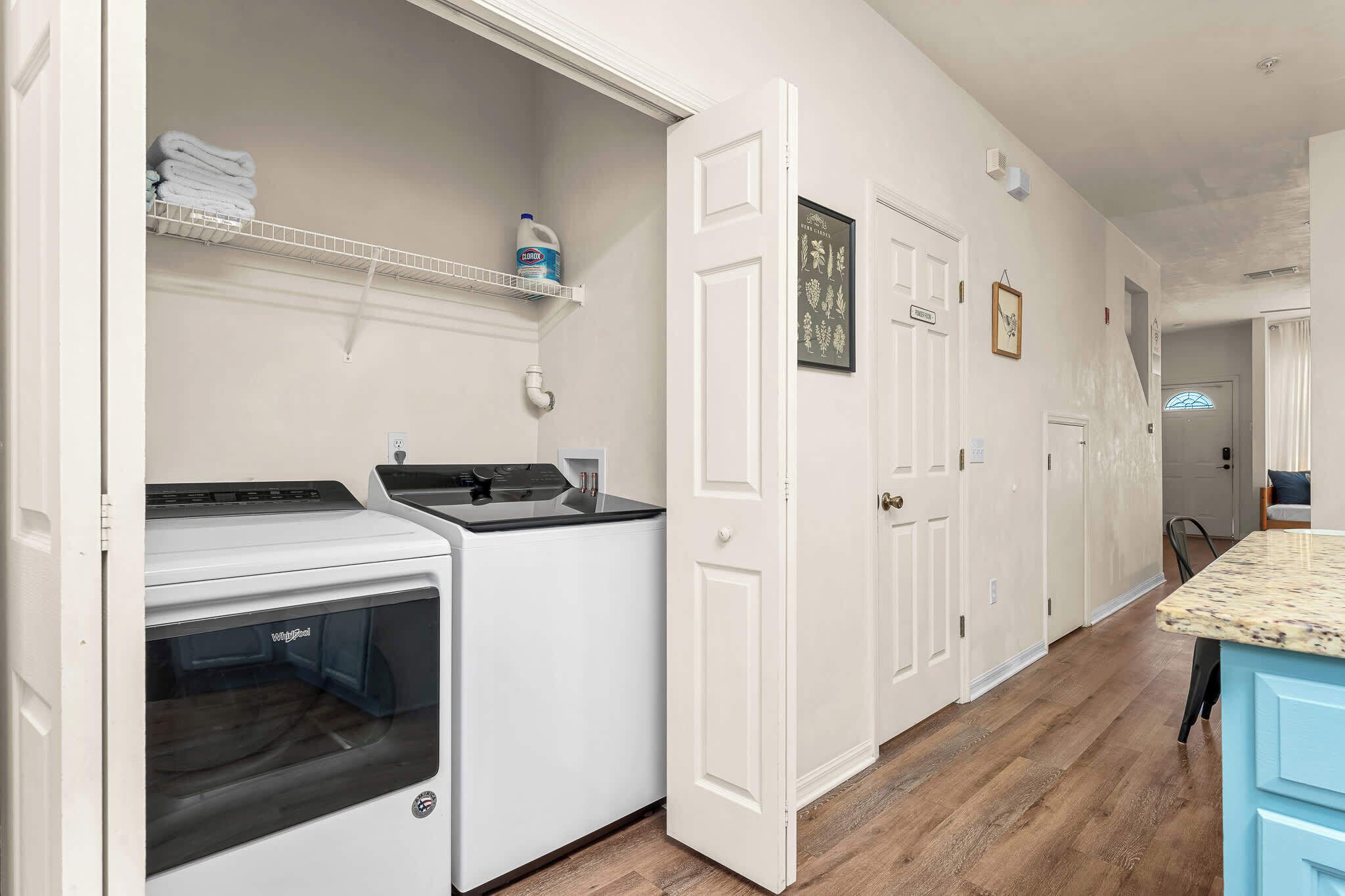 Una cocina con lavadora y secadora integradas, armarios blancos y piso de madera.