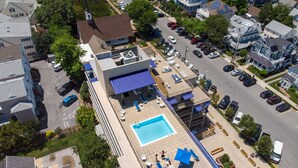 Vista aérea de una zona residencial con piscina en la azotea, sillas de descanso y un patio cubierto.