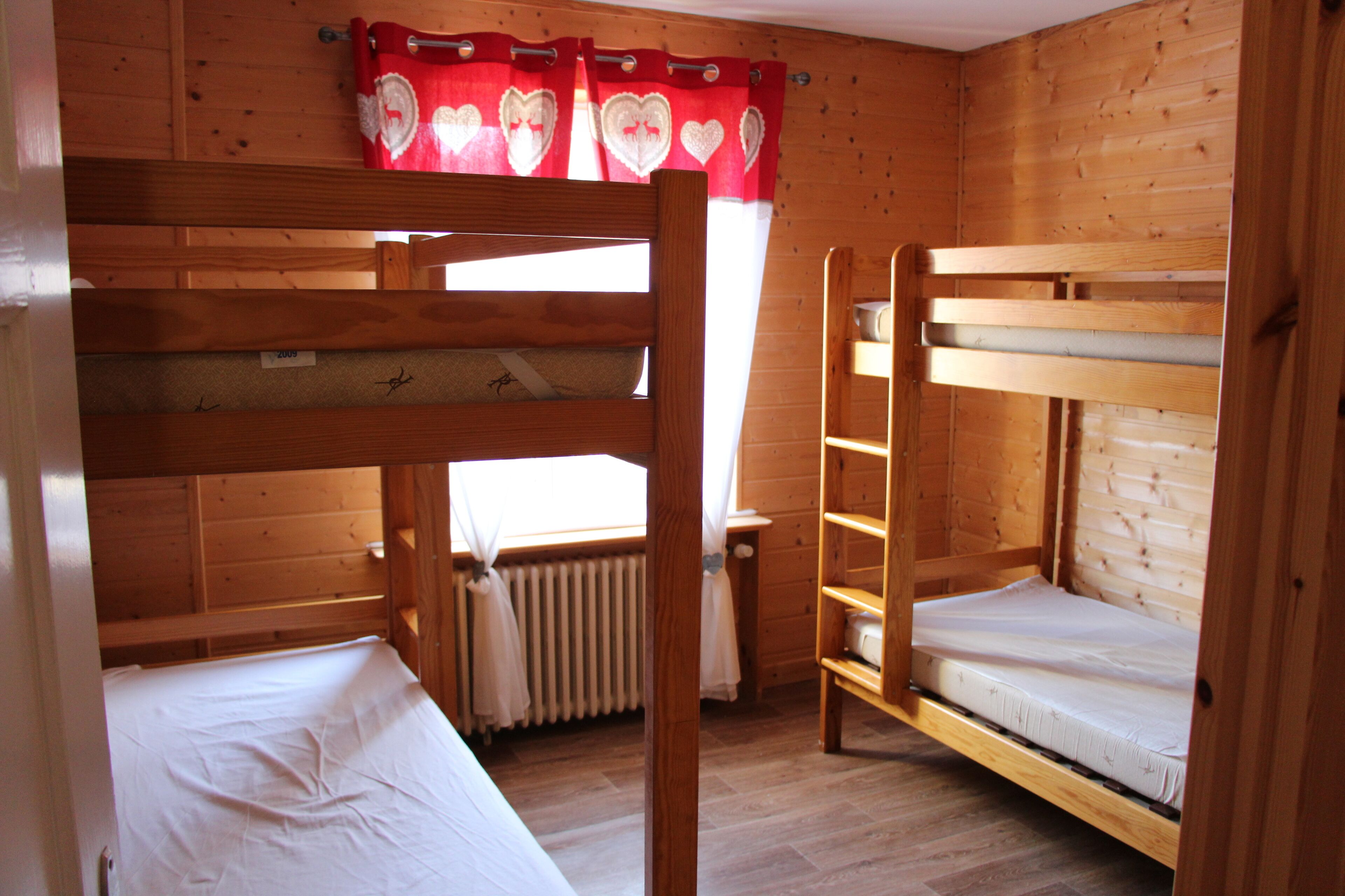 A wooden cabin with bunk beds, a window with curtains, and a radiator.