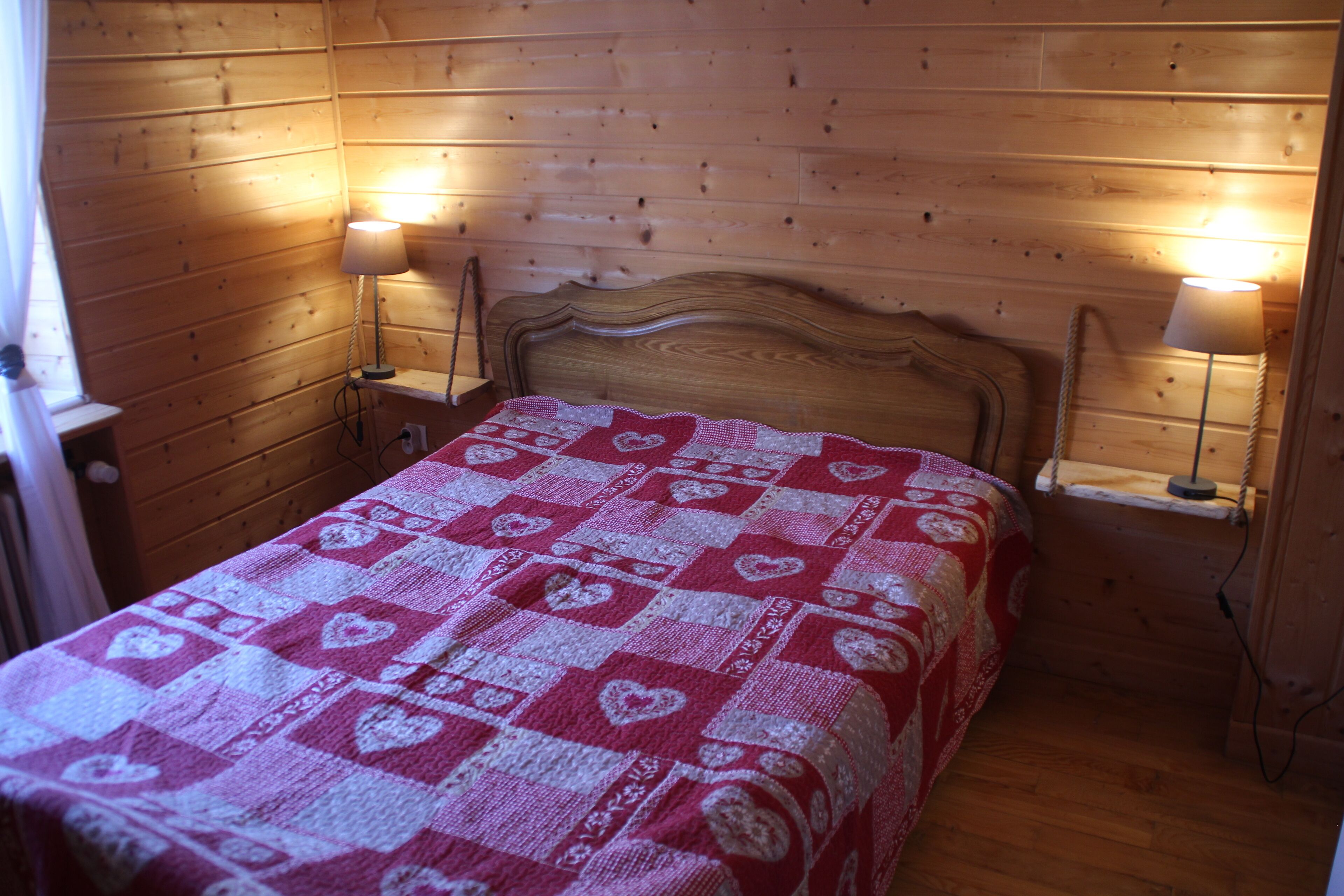 A wooden-paneled room with a bed, two bedside lamps, and a window with curtains.